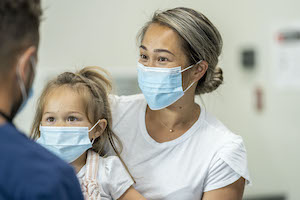 Mother and daughter visit the doctors office wearing protective face masks for the checkup to avoid the transfer of germs during COVID-19.